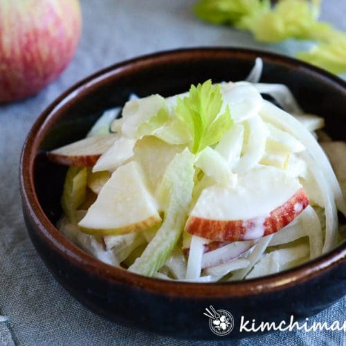 creamy apple onion celery salad plated in brown shallow bowl on blue cloth