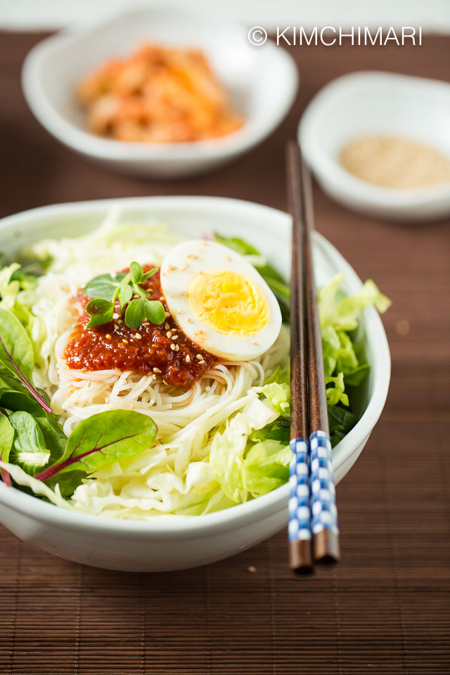 Bibim Guksu served in bowl with vegetable toppings and a side dish of kimchi