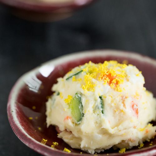 Korean potato salad served as a scoop on red bowl with grated egg yolk on top