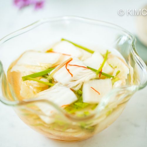 closeup of nabak kimchi in glass bowl with a place setting of spoon