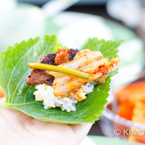 perilla leaf on hand piled with rice, pork belly, kimchi and ssamjang